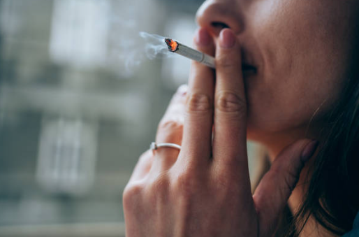 Fotografia de uma mulher fumando com cicarro na boca, acesso e com saída de fumaça.